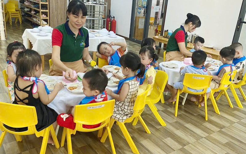Cô và các bé ngồi bàn ăn trưa với ghế vàng trong phòng ăn